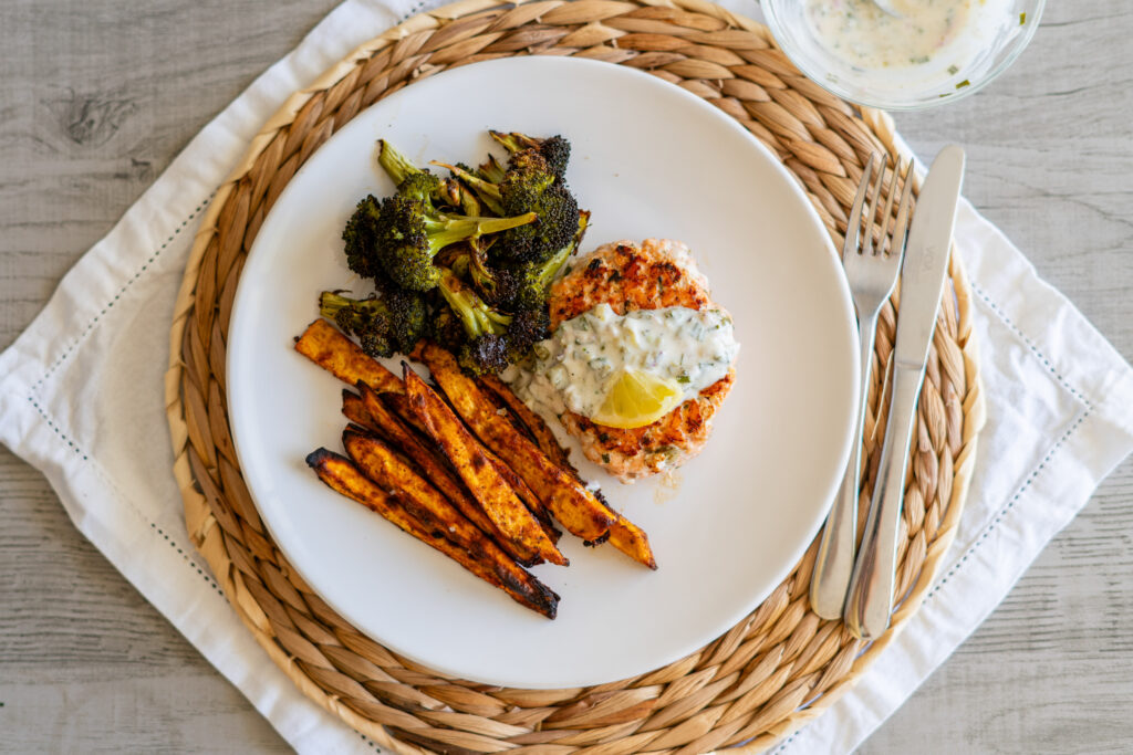a picture of a salmon burger, sweet potato fries and broccoli as a complete dinner. 